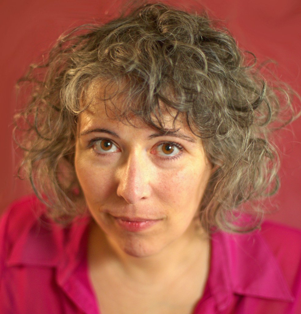 A white woman with curly greying hair and a pink shirt