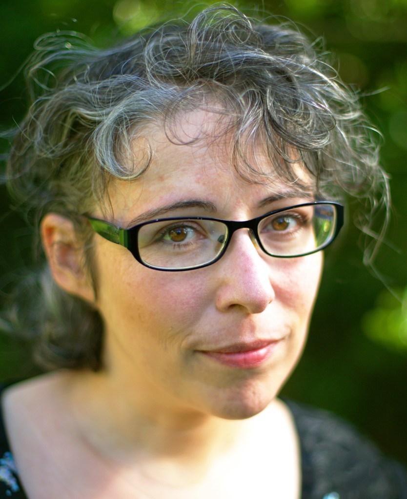 A white woman with curly greying hair and glasses